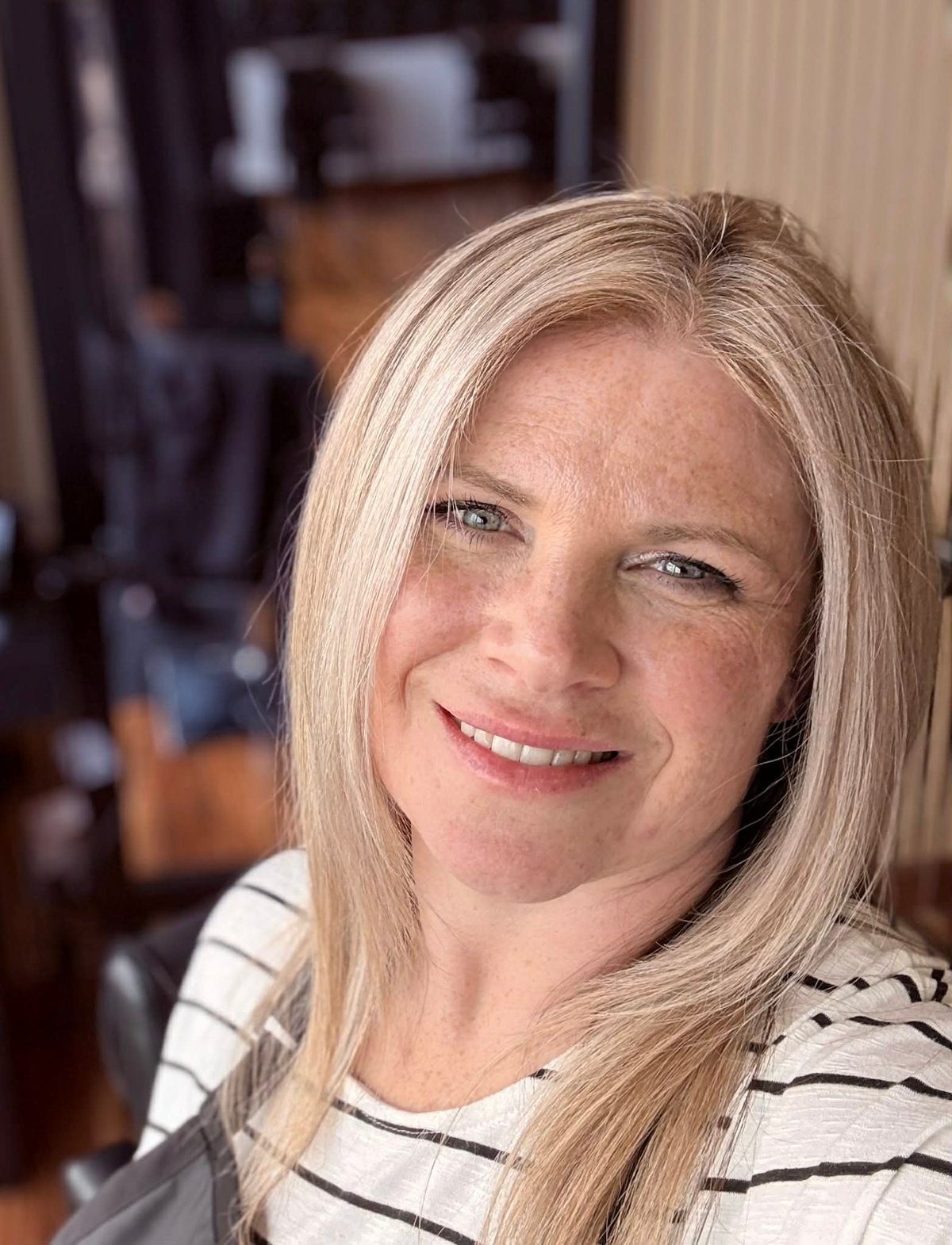 Portrait of a woman with blonde hair wearing a striped shirt, smiling at the camera indoors